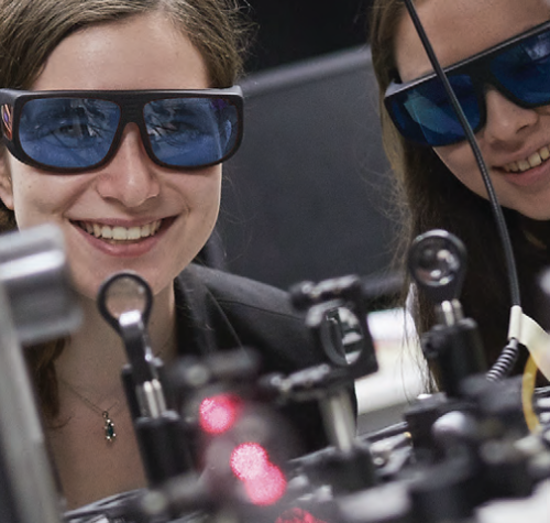 two women with goggles look through equipment with laser