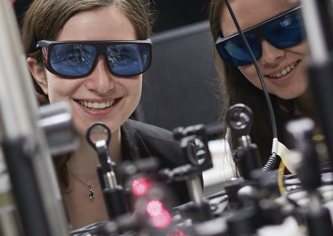 two women with goggles look through equipment with laser