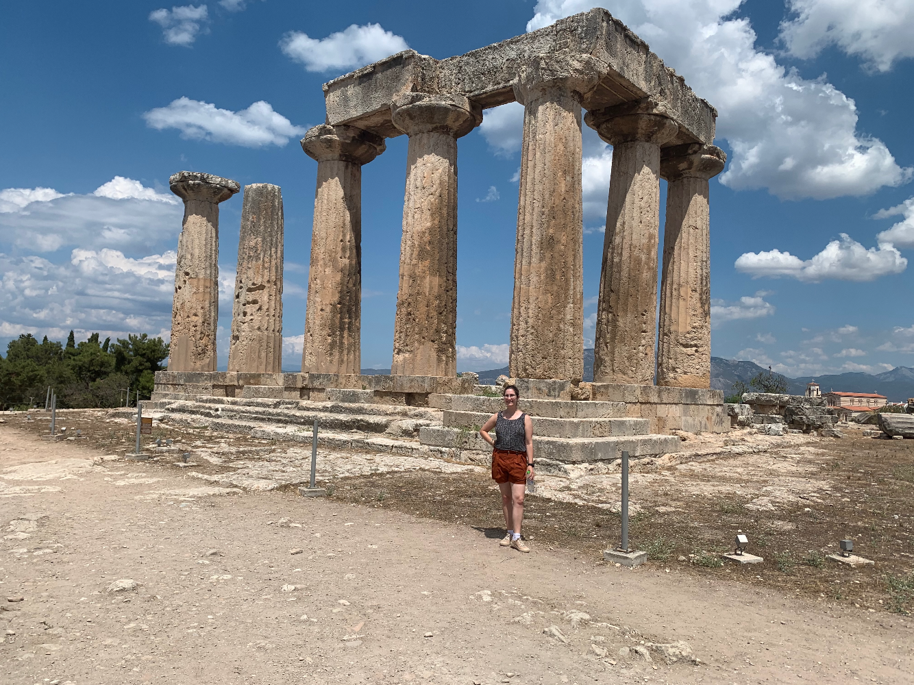 A brunette woman in baggy shorts and tank poses in front of an "L" formation of columns topped with a cornice.