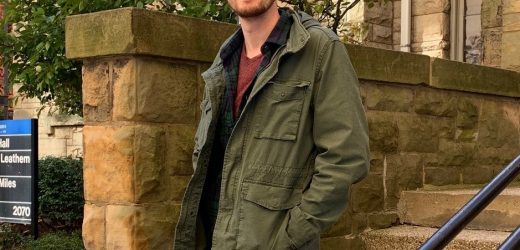 Male student stands on steps and railing near college building